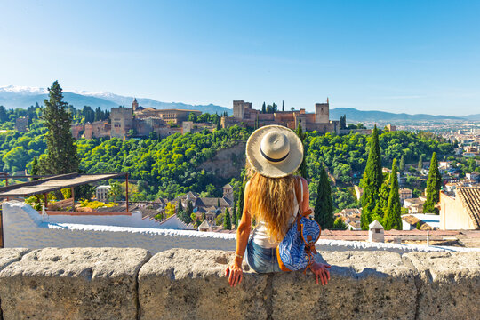 young woman with leather backpack overlooking alhambra palace in granada spain, panoramic view of the nasrid palaces and alcazaba from san nicolas viewpoint, authentic andalusian travel and heritage
