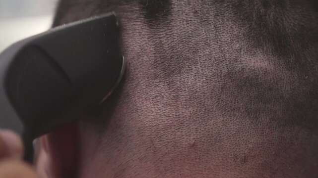 Close-up of electric hair clipper shaving a man's head for a crew cut or buzz cut in a modern barbershop or at home