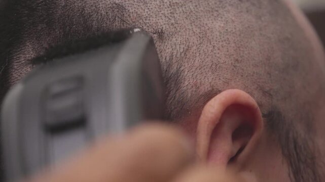 Barber giving a buzz cut to a male client in a barbershop. Close-up of an electric clipper shaving very short hair on a man's head