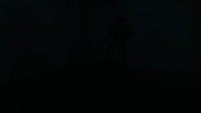 Front view wide angle shot of young man emerging from darkness and dancing expressive freestyle with fluid motions under strobing lights in dark empty concrete bunker, cinematic with copy space
