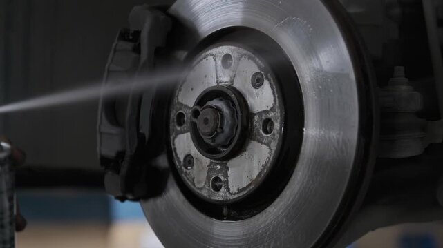 Close Up of Spraying Chemical Brake Cleaner Liquid onto a Car Disc Rotor to Clean Grease in Auto Repair Shop