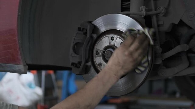 Close Up of Mechanic Hand Cleaning and Wiping a Car Brake Disc Rotor with a Rag in an Auto Repair Shop