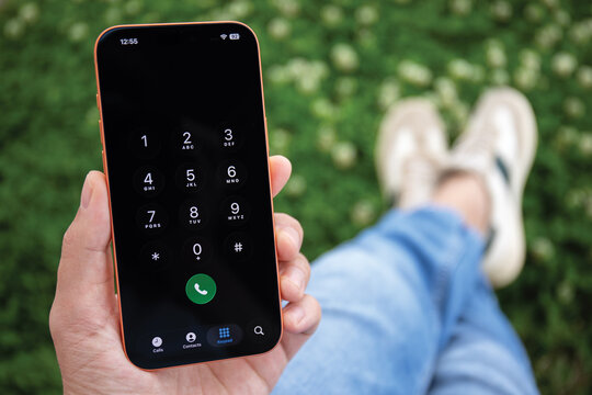 Man hand holding Phone Apple iPhone 17 Pro Max Cosmic Orange outdoor, displaying phone dialer keypad with numbers and green call button on the screen IOS 26
