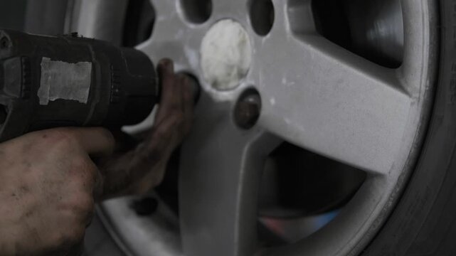 Close Up of Mechanic Using a Pneumatic Air Impact Wrench to Change a Car Wheel Rim Tire in a Service Shop