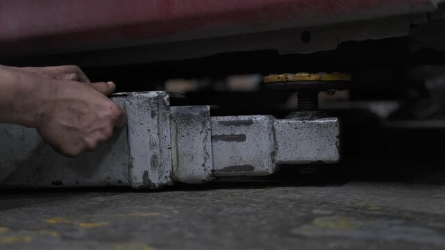 Close Up of Hydraulic Hydraulic Lift Arm Lifting and Raising a Red Car in an Auto Repair Workshop