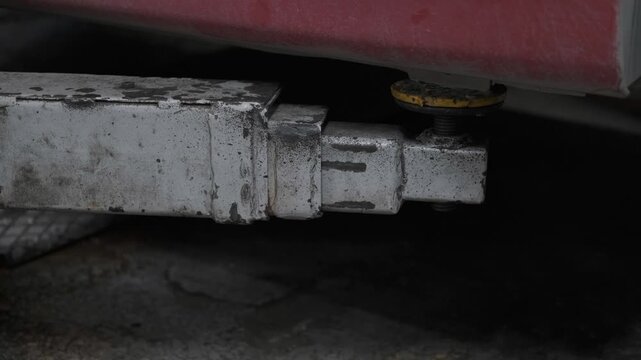 Close Up of Hydraulic Hydraulic Lift Arm Lifting and Raising a Red Car in an Auto Repair Workshop