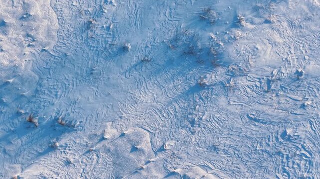 Drone video showcases intricate patterns on a snow-blanketed terrain, capturing untouched textures and subtle shadows in soft golden hour sunlight. No people or animals present.