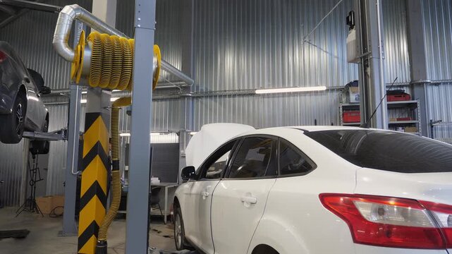 An auto mechanic works in an auto repair shop. He repairs something under the hood. The car is lifted onto a lift at the service station. The process of working in a modern service station.