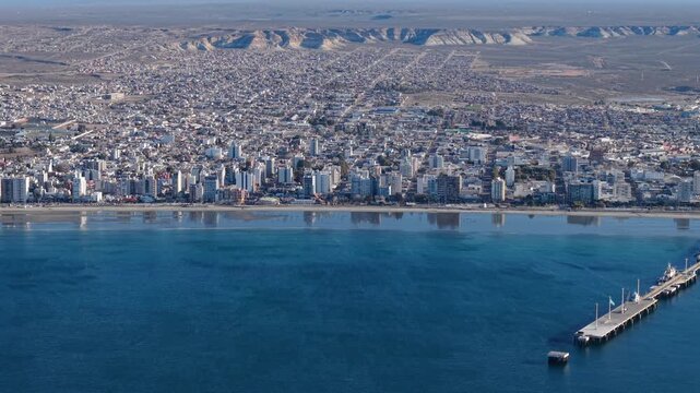 Puerto Madryn Chubut Argentina along Golfo Nuevo shows urban waterfront and Muelle Comandante Luis Piedra Buena with Patagonian plateau mesas of Somuncur&aacute; foreland in background, drone lateral slide