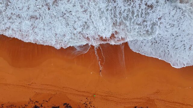 Top View White Foam Waves on Orange Sand Beach Panama. An overhead shot captures white ocean foam spreading across a vivid orange sandy beach from above.