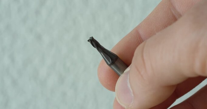 Macro close-up of a small sharp milling cutter held between fingers, showing precision tooling, metalworking, machining detail, and industrial cutting equipment.