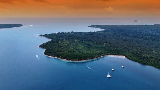 Aerial Sunset View Forested Island with Catamarans Bocas del Toro. Three white catamarans anchor near a forested island beach under a vivid orange and red sunset sky.
