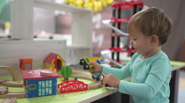 Young child playing with toy train. Boy, plays, railroad, toys carriages, train, son. A train with carriages and a boy playing with it. The photo is of a child lifestyle playing with a toy train.