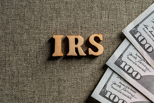 IRS wooden letters with US hundred dollar bills on fabric background, top view. Concept of American taxation with wooden letters IRS and hundred dollar bills on textured background