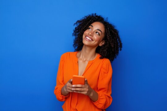 The woman in orange blouse smiling while holding a smartphone against a blue background