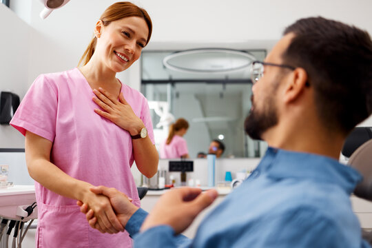 Friendly dentist shaking hands with satisfied patient after appointment