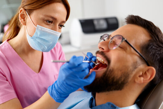 Close up of female dentist examining male patient teeth with dental instruments during oral healthcare visit