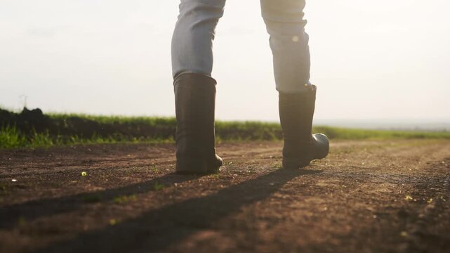 A person walking on a dirt road. Farmer goes on a road at sunset. Farmers walk close up on their legs in agriculture. An individual strolling along a lifestyle dusty path.