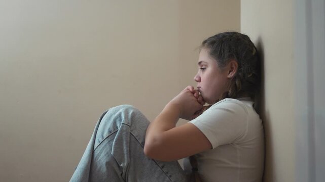 Young girl sitting on the floor. Sad child sits on a corner and is punished. A teenage girl is traumatized by a violent incident. A little lifestyle girl sitting on the ground.