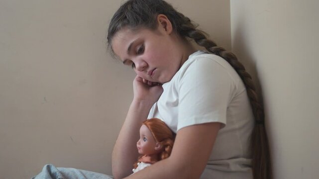 Young girl sitting on the floor with her doll. Girl punished with a doll in a corner. A teenage girl is traumatized by violence and psychological lifestyle trauma. A young girl is on the floor with.