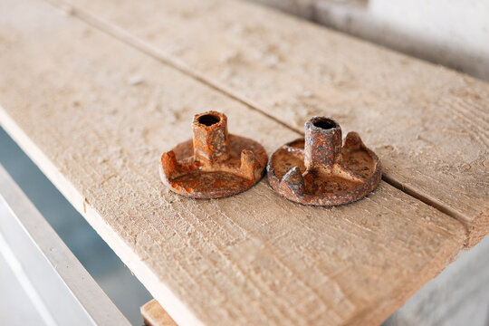 Two rusty metal wing nuts used for concrete formwork tie rods resting on a rough wooden plank at a building construction site.