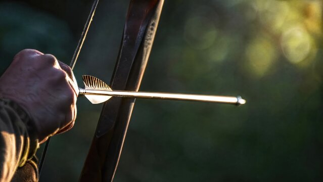 A bow with taut string and nocked arrow against a blurred natural background. 
