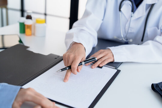 Doctor explaining treatment plan and obtaining informed consent while patient signing consent form in hospital.