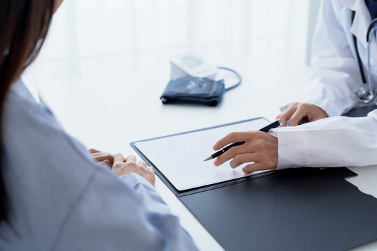 Doctor explaining treatment plan and obtaining informed consent while patient signing consent form in hospital.