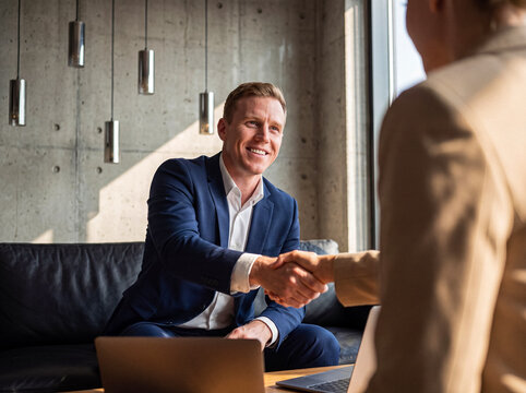 Confident businessman in a suit shaking hands with an associate, finalizing a new business partnership agreement.