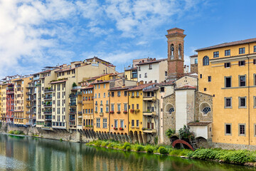 Obraz premium Colorful buildings lining the Arno River in medieval Florence under a blue sky with fluffy clouds