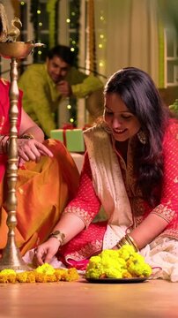 Decorating flower rangoli around samai, Indian young girl senior mother in traditional wear joyfully preparing for Hindu festival Diwali celebration indoors in evening with diya and colorful design