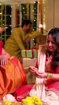 Decorating flower rangoli around samai, Indian young girl senior mother in traditional wear joyfully preparing for Hindu festival Diwali celebration indoors in evening with diya and colorful design