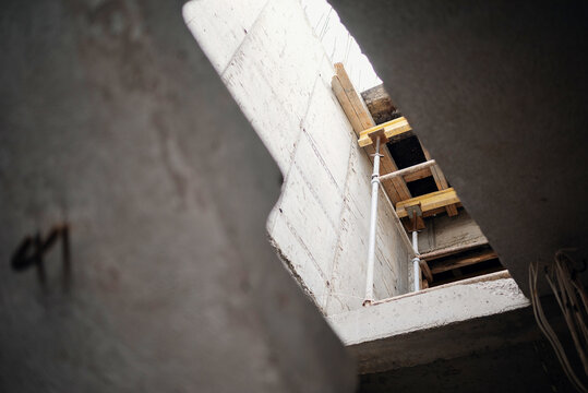 A low angle view looking up through a raw concrete ceiling opening at metal shoring props and yellow wooden formwork beams at a construction site.