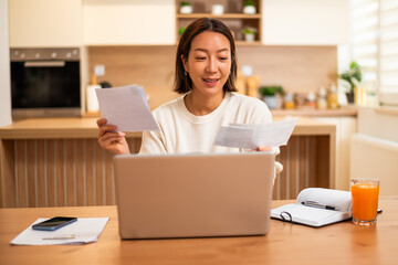 Adult Asian woman holding financial bills and statements, calculating her expenses.
