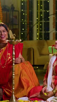 Lighting samai diya indoors during Diwali, Indian family of four including senior mother in saree, father, young girl, and husband smiling together celebrating Hindu festival with joy and tradition