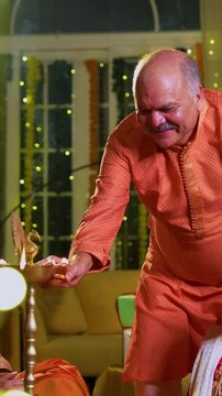Lighting samai diya indoors during Diwali, Indian family of four including senior mother in saree, father, young girl, and husband smiling together celebrating Hindu festival with joy and tradition