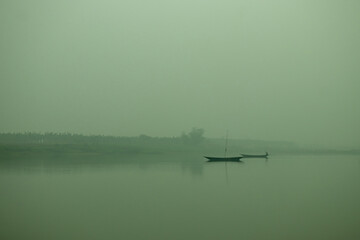 A misty morning over a calm river, silhouetted fishing boats drift © mssozib