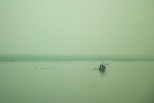 Two fishermen cast a long net across a misty river