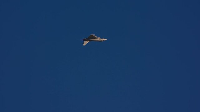 Military fighter jet in steep banking turn at altitude against deep blue sky showing topside of fuselage, slow motion capture
