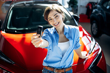 Happy woman holding new car keys, celebrating successful vehicle purchase at a dealership,...