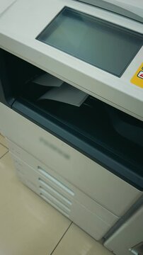 Vertical close-up of a modern office multifunction printer copying and printing documents