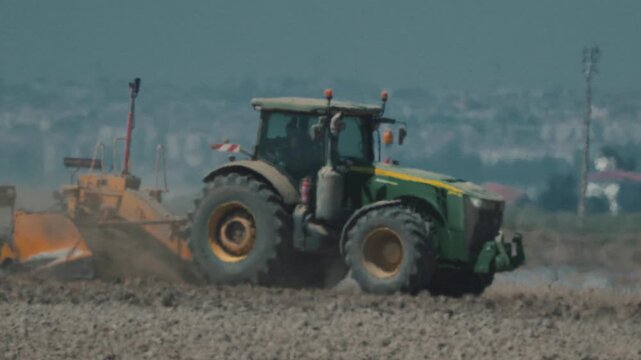Tractor plows field in rural area during sunny day with clear sky and distant hills in background