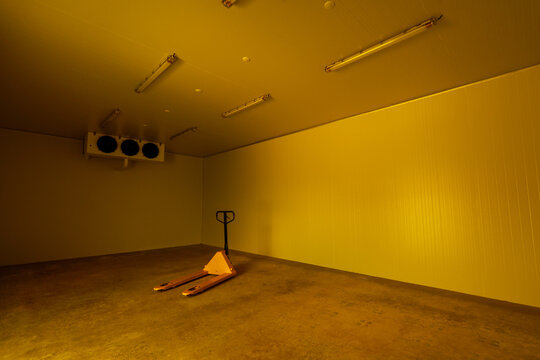 Empty yellow cold storage warehouse room with solitary manual pallet jack on concrete floor expressing eerie lonely abandoned atmosphere inside industrial facility