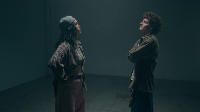Cinematic slow motion shot of two dancers male and female entering shot and facing each other, underground dance stand off in dark industrial studio, copy space