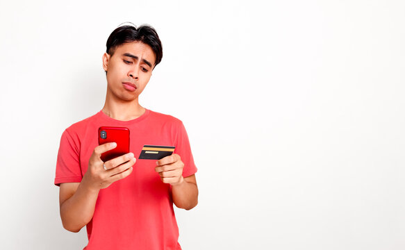 Doubtful young asian man looking at smartphone while holding credit card for financial problem and difficult online payment transaction concept