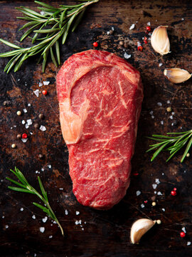 Raw ribeye beef steak with fresh rosemary garlic sea salt and peppercorns on dark rustic background for gourmet cooking concept. Close up. Top view.
