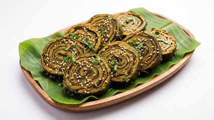 Rolled steamed savory parcels made from colocasia leaves, sprinkled with white sesame seeds © Kumuthini