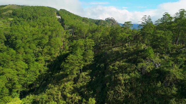 Aerial rise above Marlboro Hill in Sagada reveals lush pine forest slopes, rocky mountain peaks, rolling grasslands and sweeping valley views under dramatic clouds in Mountain Province
