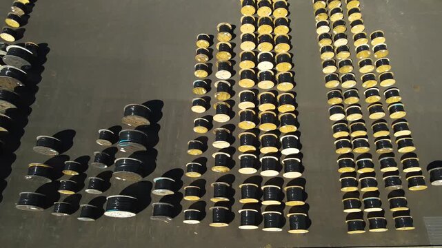 Many large wooden and metal cable drums storing electrical or fiber optic wires organized in rows at an industrial plant, creating a geometric pattern from an aerial top down perspective
