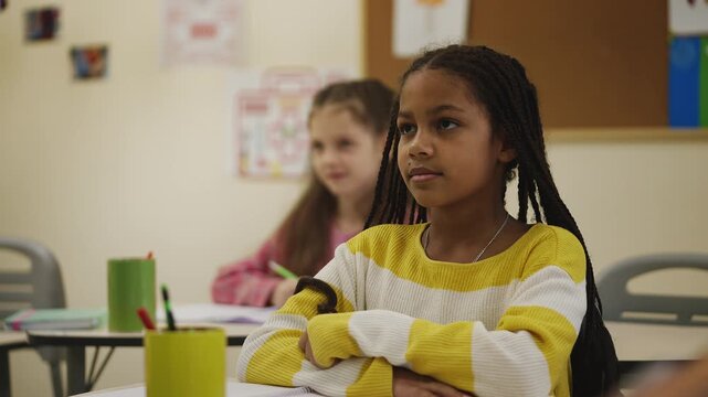 African American girl raising hand to answer teacher's question in classroom